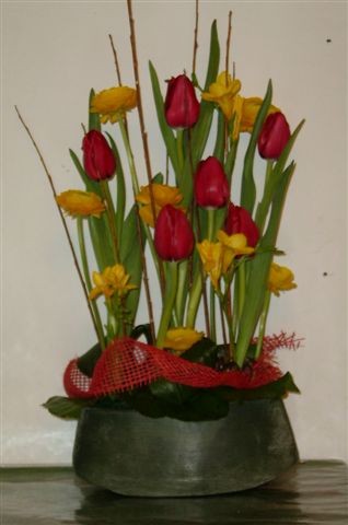 composition piqu�e dans une poterie (mod�le selon disponibilit� en magasin) fleurs piqu�es en parall�le comprenant tulipes, freesias, renoncules dans des tons jaunes, orang�s et rouge